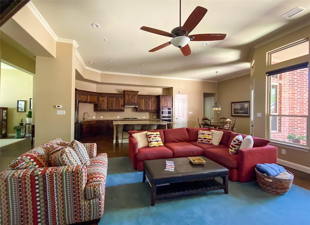 living area with ceiling fan, visible vents, wood finished floors, baseboards, and ornamental molding