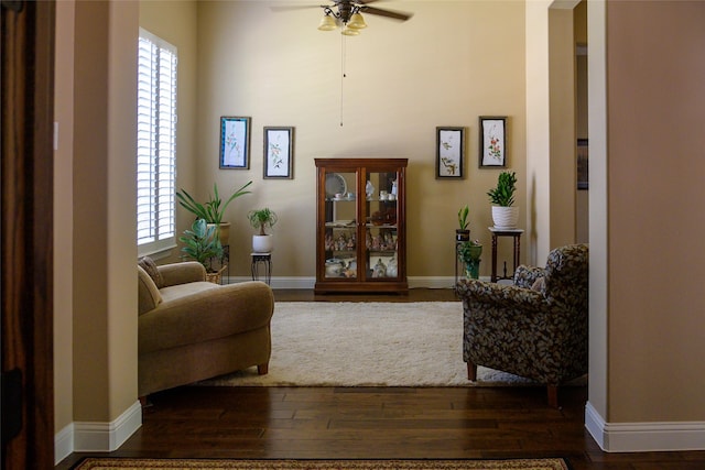 living area with dark wood-style flooring, a ceiling fan, baseboards, and a towering ceiling