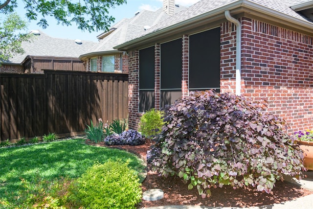 view of side of home featuring fence, a shingled roof, a chimney, and brick siding