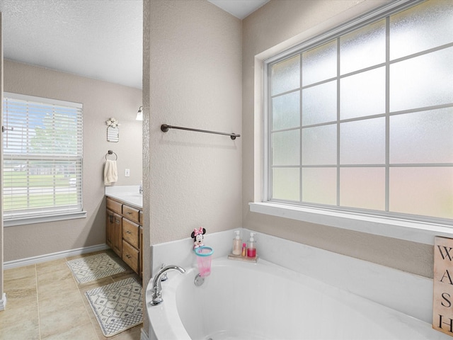 bathroom featuring vanity, a textured wall, baseboards, and a bath