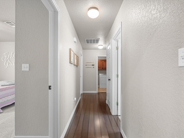 hallway featuring washer / clothes dryer, a textured wall, visible vents, and hardwood / wood-style floors