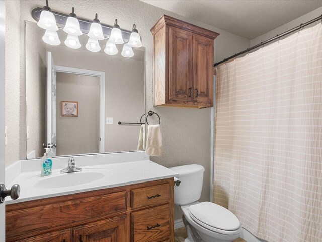 bathroom featuring toilet, a textured wall, a shower with curtain, and vanity