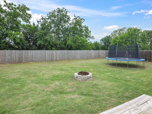 view of yard featuring a fenced backyard, a trampoline, and an outdoor fire pit
