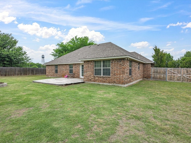 back of property featuring a shingled roof, brick siding, a deck, a fenced backyard, and a lawn