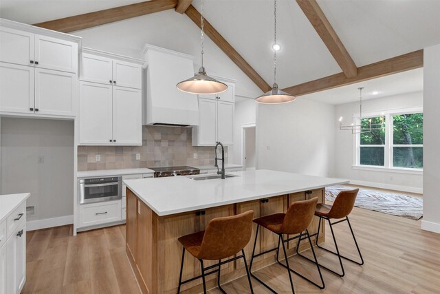 kitchen with a sink, light countertops, white cabinets, beamed ceiling, and light wood-style floors