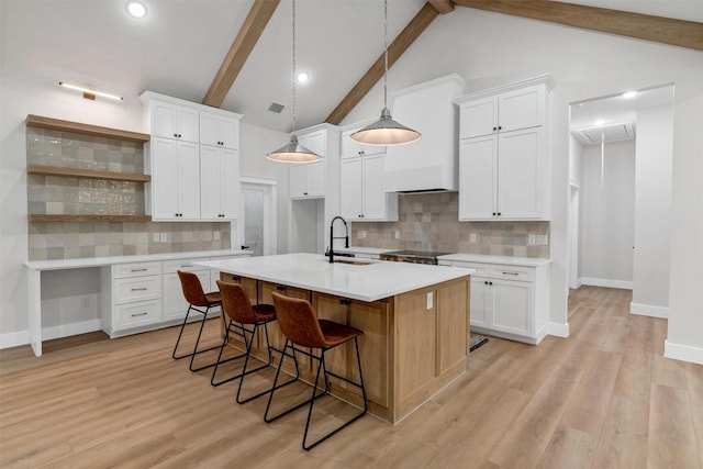 kitchen with open shelves, beam ceiling, an island with sink, a sink, and backsplash