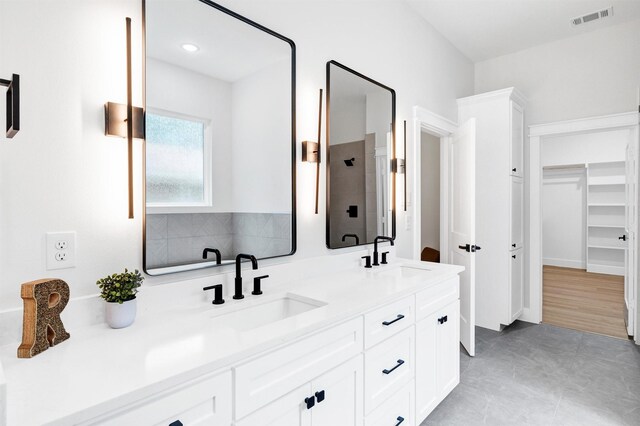bathroom featuring visible vents, a sink, a stall shower, and double vanity