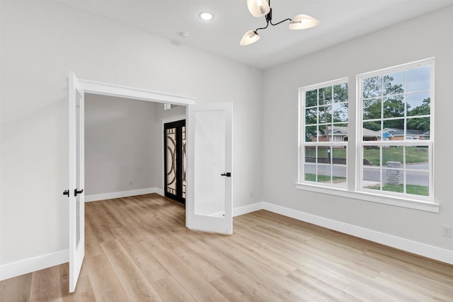 unfurnished room with baseboards, an inviting chandelier, and light wood-style floors