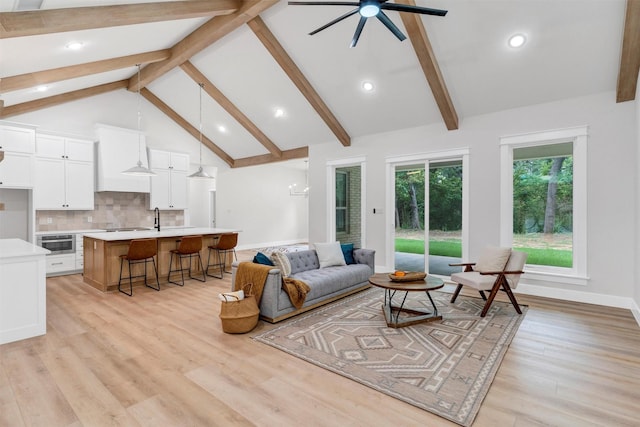 living room with beam ceiling, light wood-style floors, high vaulted ceiling, a ceiling fan, and baseboards