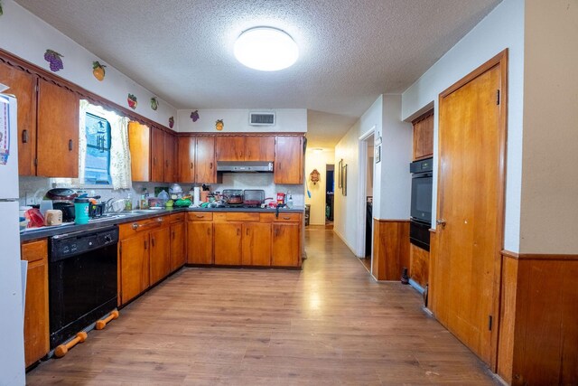 kitchen with a textured ceiling, visible vents, brown cabinets, black appliances, and under cabinet range hood