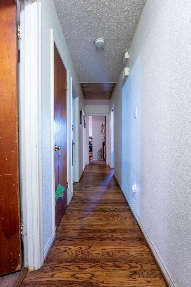 hallway featuring baseboards, a textured ceiling, a textured wall, and wood finished floors