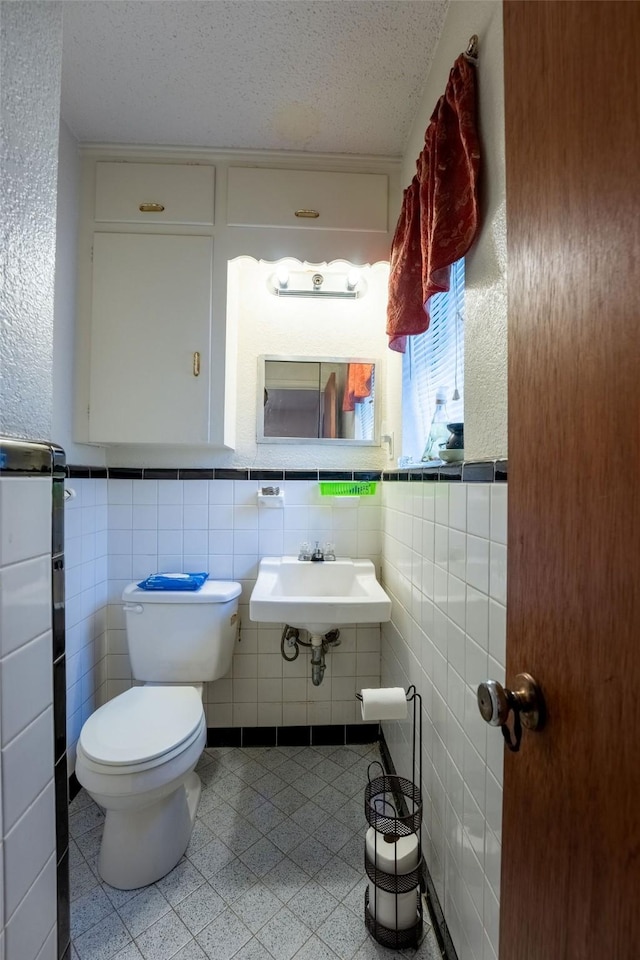 bathroom with a sink, a textured ceiling, toilet, and tile walls