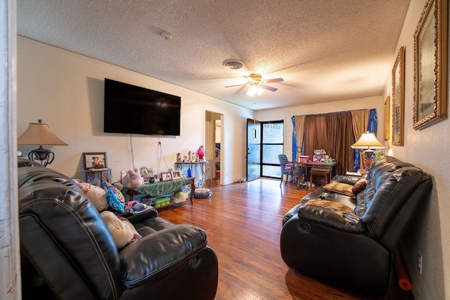 living area with a textured ceiling, ceiling fan, wood finished floors, and visible vents