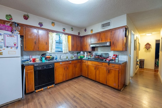 kitchen featuring visible vents, freestanding refrigerator, black dishwasher, under cabinet range hood, and brown cabinets