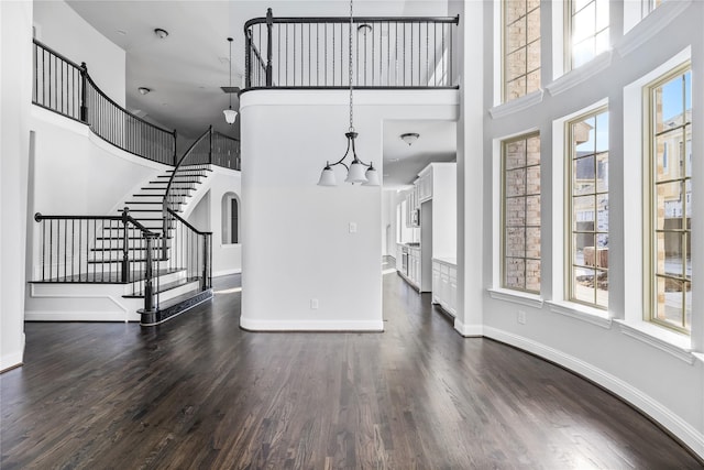 unfurnished living room with stairway, dark wood-style floors, a chandelier, and a towering ceiling
