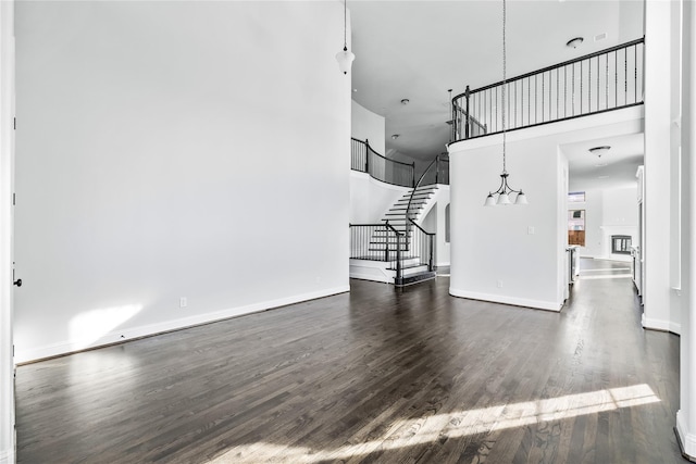 unfurnished living room featuring stairway, baseboards, a high ceiling, and dark wood-type flooring