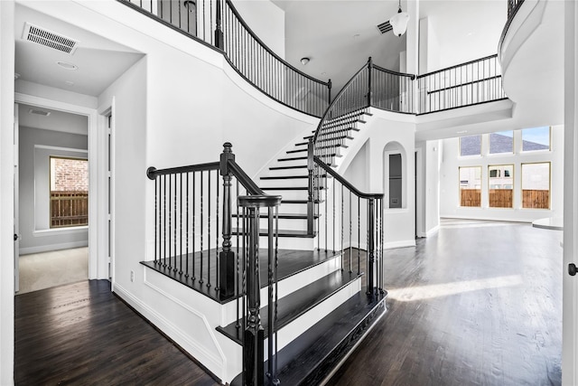 stairs with visible vents, arched walkways, a towering ceiling, and wood finished floors