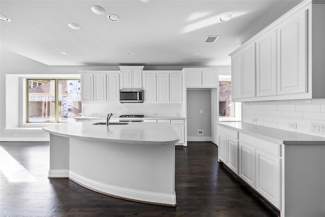 kitchen featuring visible vents, an island with sink, stainless steel microwave, white cabinets, and a sink