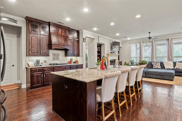 8225 Bonny Bank, The Colony, TX 75056 - kitchen featuring crown molding, a breakfast bar, open floor plan, a fireplace, and light stone countertops