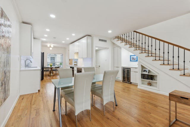 dining room featuring a dry bar, light wood-style flooring, stairway, and wine cooler