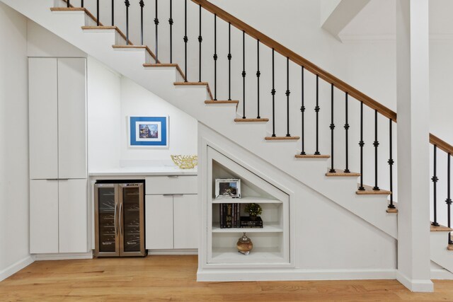 stairs featuring beverage cooler, a dry bar, baseboards, and wood finished floors