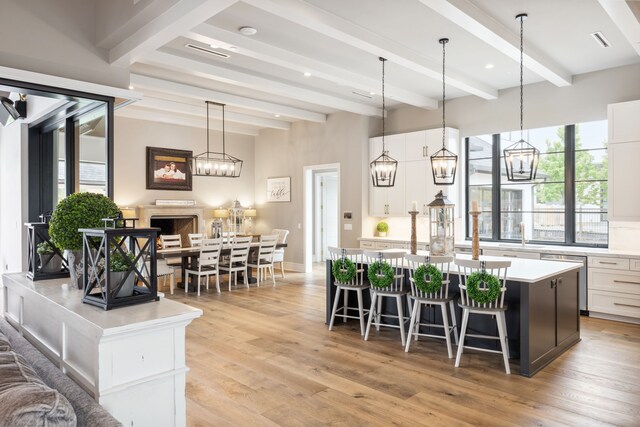 kitchen featuring stainless steel dishwasher, an island with sink, beam ceiling, and light countertops