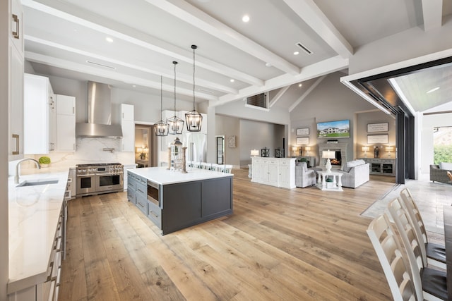 kitchen with a large island, open floor plan, wall chimney exhaust hood, a sink, and double oven range