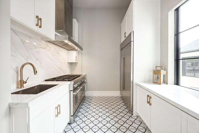 kitchen with a sink, wall chimney exhaust hood, white cabinetry, decorative backsplash, and premium appliances