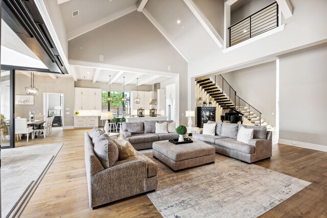 living room featuring light wood-style floors, high vaulted ceiling, stairway, and beamed ceiling