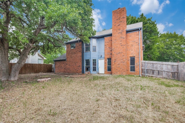 back of house with a lawn, brick siding, a chimney, and a fenced backyard