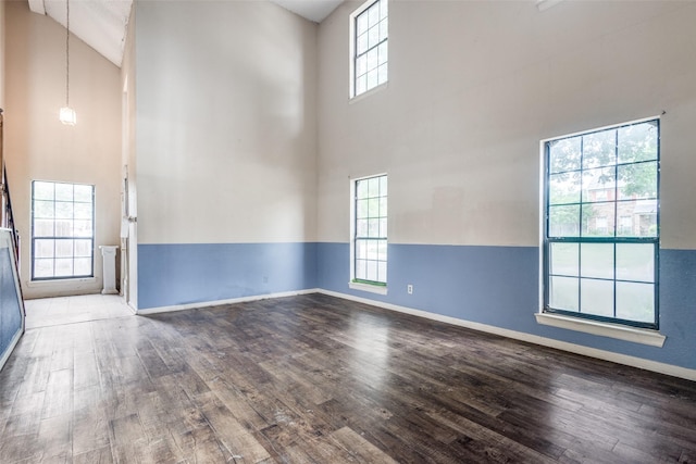unfurnished room featuring baseboards, wood finished floors, and high vaulted ceiling