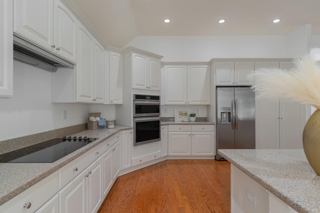 kitchen featuring light stone countertops, light wood-type flooring, white cabinetry, appliances with stainless steel finishes, and vaulted ceiling