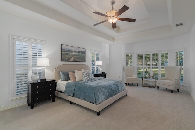 bedroom with light colored carpet, a tray ceiling, and multiple windows