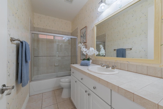 full bathroom with tile patterned flooring, vanity, toilet, wallpapered walls, and bath / shower combo with glass door