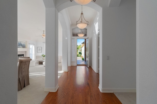 hall with baseboards, arched walkways, wood finished floors, and a wealth of natural light