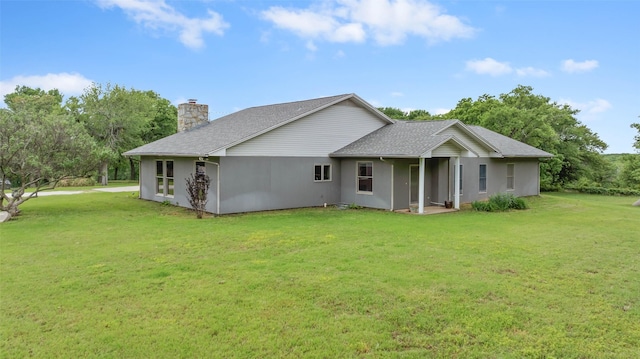 back of property featuring a lawn, a chimney, a shingled roof, and stucco siding
