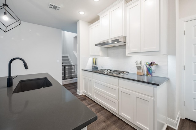 kitchen with dark countertops, a sink, stainless steel gas cooktop, under cabinet range hood, and visible vents
