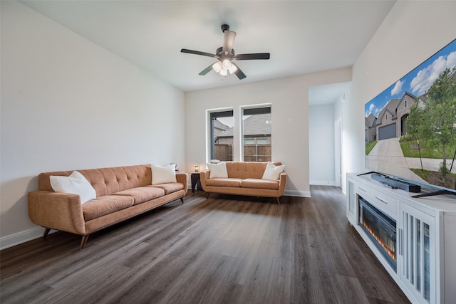 living room with baseboards, dark wood finished floors, ceiling fan, and a glass covered fireplace