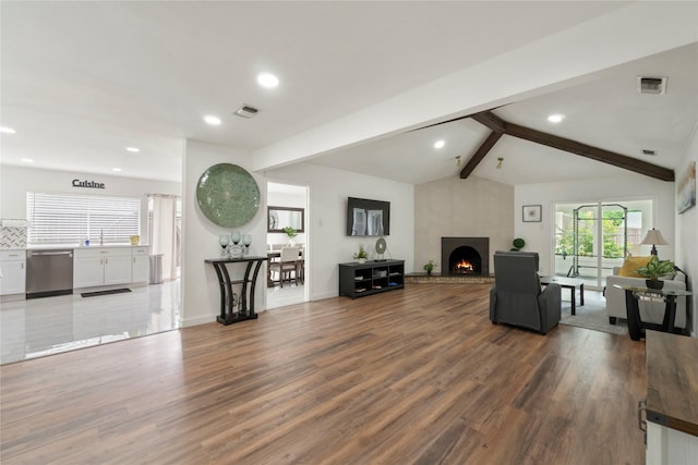 living area featuring vaulted ceiling with beams, visible vents, wood finished floors, and a fireplace