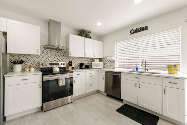 kitchen featuring appliances with stainless steel finishes, a sink, wall chimney exhaust hood, white cabinetry, and decorative backsplash
