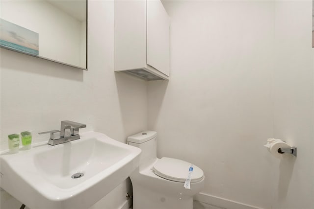 half bath featuring baseboards, a sink, and toilet