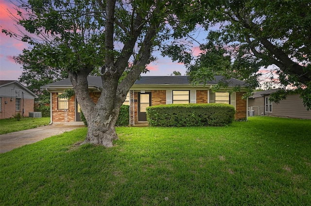 view of front of property featuring brick siding, driveway, central AC unit, and a front yard