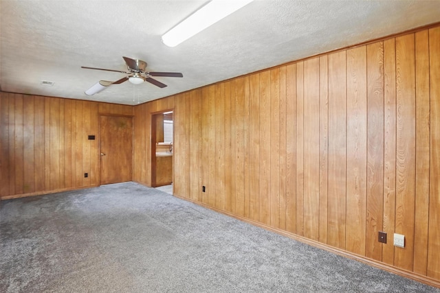 spare room with a ceiling fan, a textured ceiling, visible vents, carpet floors, and wooden walls