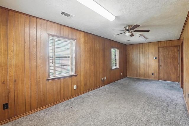 carpeted empty room with visible vents, wood walls, a textured ceiling, and ceiling fan