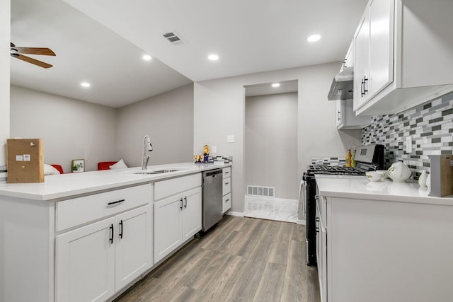kitchen featuring appliances with stainless steel finishes, a sink, a peninsula, under cabinet range hood, and visible vents