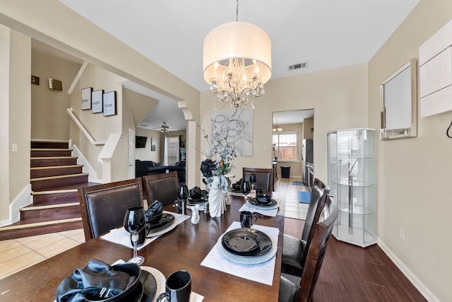 dining area featuring visible vents, wood finished floors, stairway, baseboards, and ceiling fan with notable chandelier
