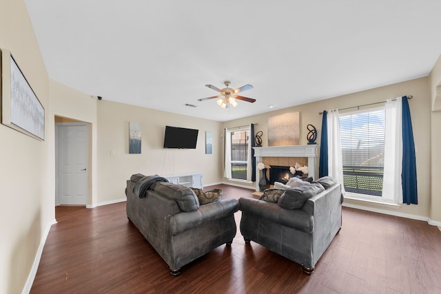 living room featuring a tiled fireplace, baseboards, a ceiling fan, and dark wood finished floors