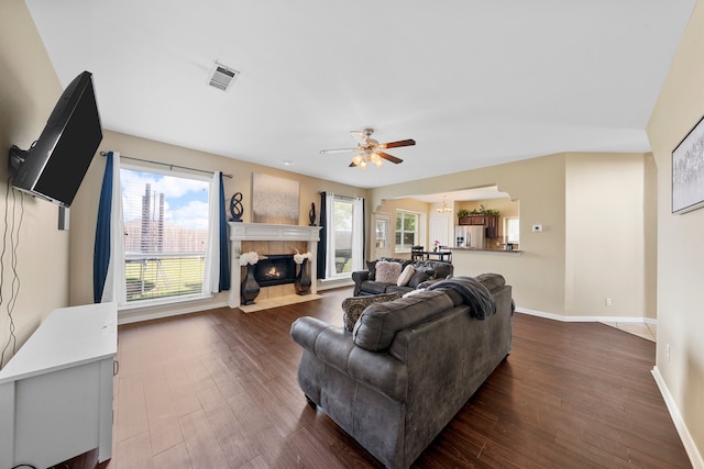 living room featuring visible vents, a fireplace, baseboards, dark wood-style floors, and a ceiling fan