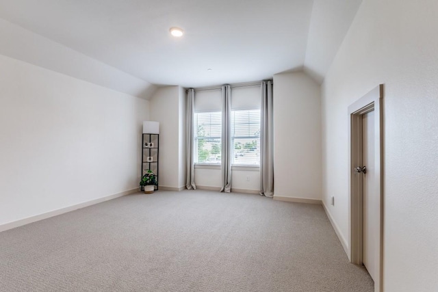 unfurnished room featuring baseboards, vaulted ceiling, and light carpet