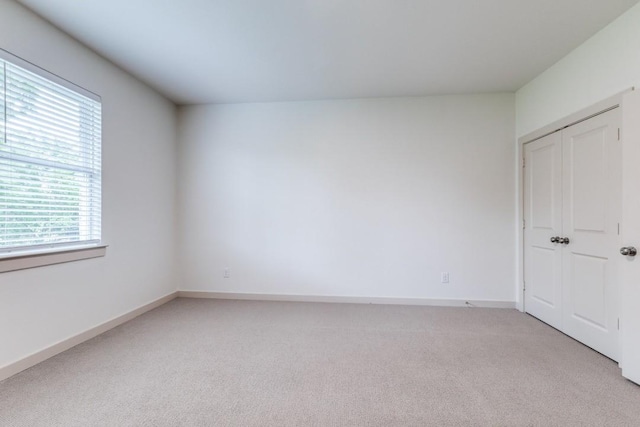 unfurnished bedroom with baseboards, light carpet, and a closet